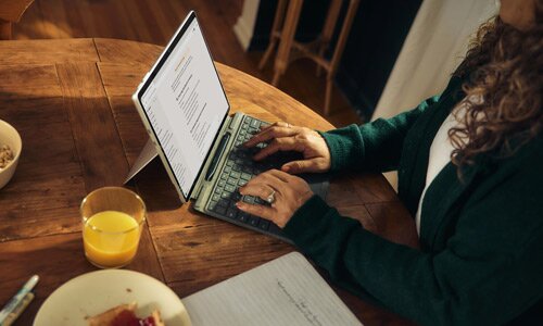 Woman typing on a laptop in a house with breakfast plate beside her.