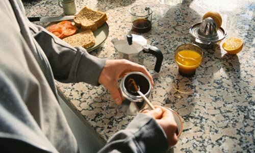 A persons' hands making breakfast with orange juice, toast and coffee.