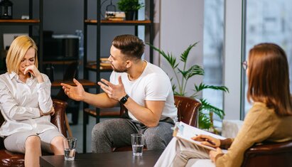 illustration of couples therapy session, a man is speaking with his hands and a woman looks visibly upset. the practitioner is facing the couple with a clipboard