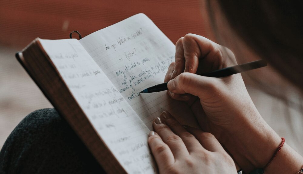 close up person using a gratitude letter template to write a letter in a journal