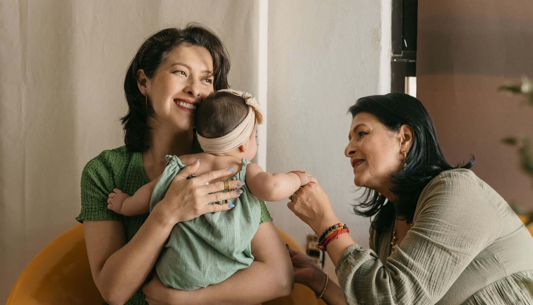 woman holding a baby, with another woman holding the baby's hand