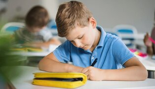little boy at school writing and using an ADHD worksheet for kids at his desk