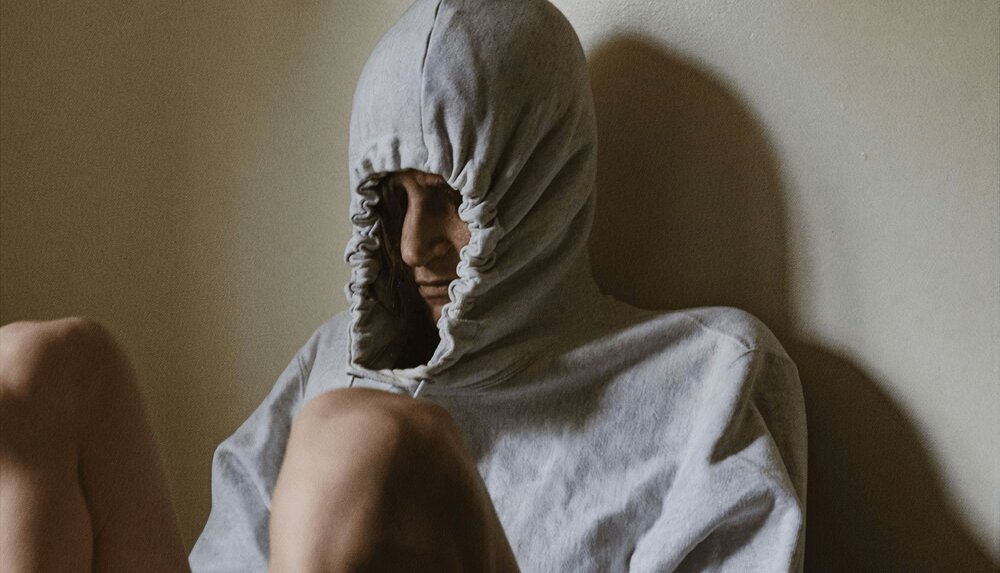 person sitting down and pulling their hood tight over their head avoiding a situation