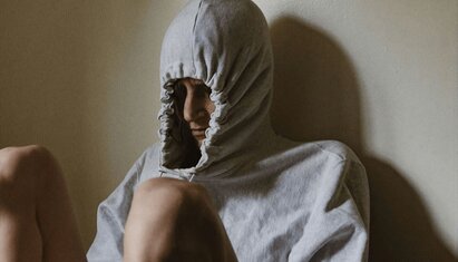 person sitting down and pulling their hood tight over their head avoiding a situation