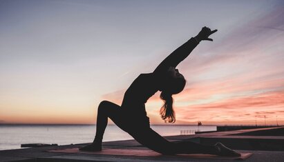 silhouette of person doing yoga, a coping skill for addiction, in front of a sunset