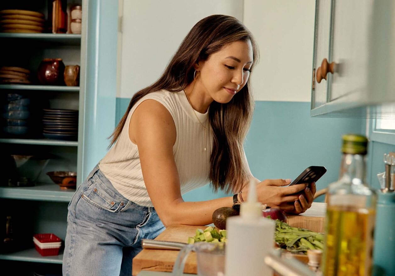 woman on her phone in a kitchen with chopped vegetables on the counter