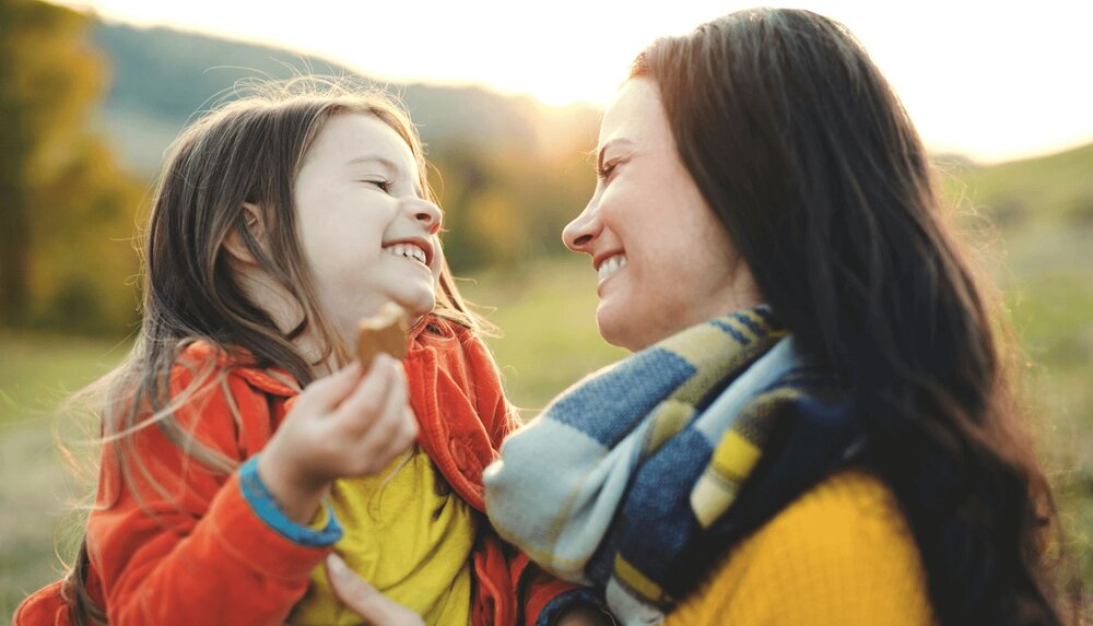 adult holding child and smiling as she helps her through a how I feel worksheet