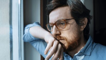 man with glasses looking out window and reading social anxiety worksheet