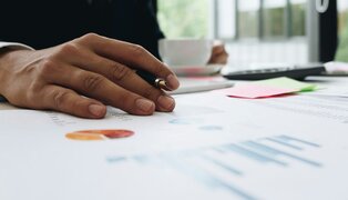 person's hand holding a pen, over papers containing reports and charts
