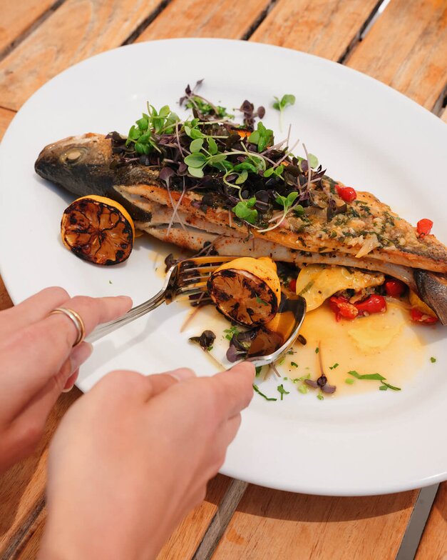 The Grilled Sea Bass dish plated for a guest sitting on the rail with a glass of wine