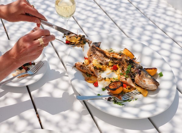 The Grilled Sea Bass dish plated for a guest sitting on the rail with a glass of wine