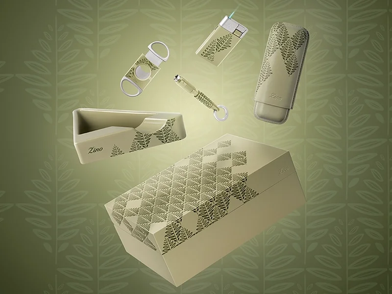 Elegantes Zino Z-Collection Accessoire-Set vor grünem Blätterhintergrund mit Humidor, Feuerzeug, Zigarrenschneider und geometrischem Aschenbecher.
