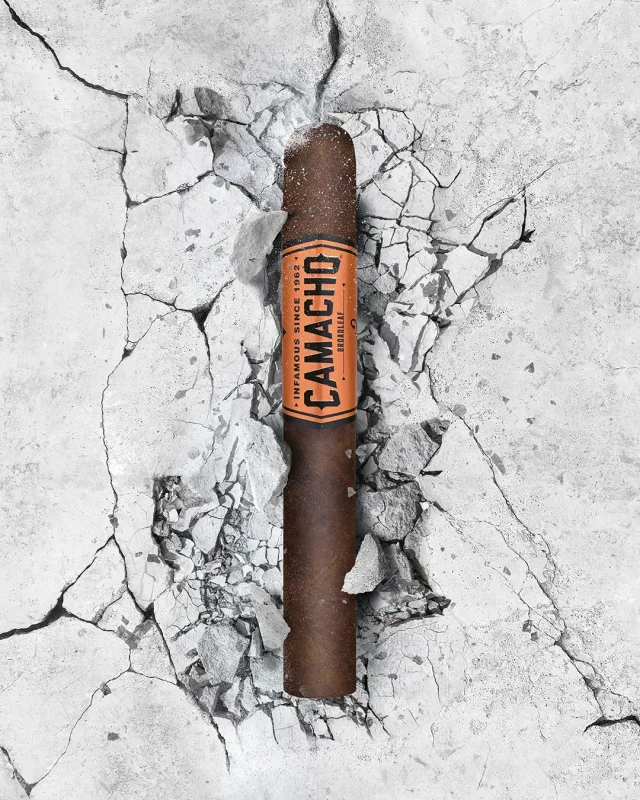 A Camacho cigar with a bold black and orange band, resting on a textured dark stone surface.