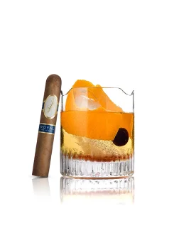Royal Release Robusto Zigarre neben einem Whiskeyglas mit Orangenschale und Kirsche auf weißem Hintergrund.