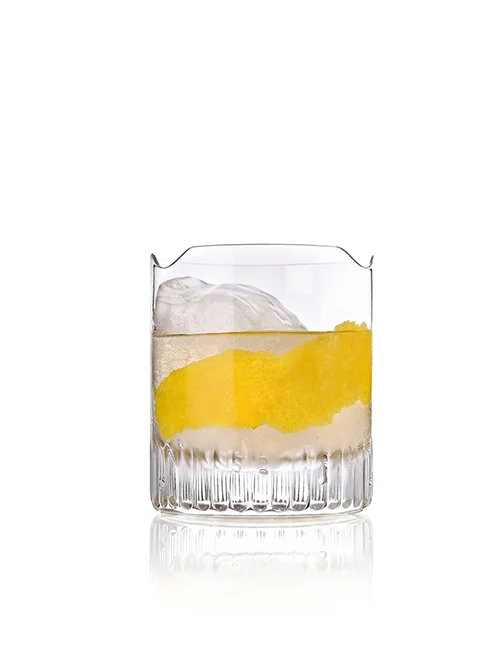 Whiskeyglas mit Zitronenzeste und Eis auf reflektierender Oberfläche.