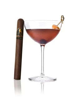 Late Hour Winston Churchill-Zigarre neben einem roten Late-Night-Coffee-Cocktail mit Orangenzeste.