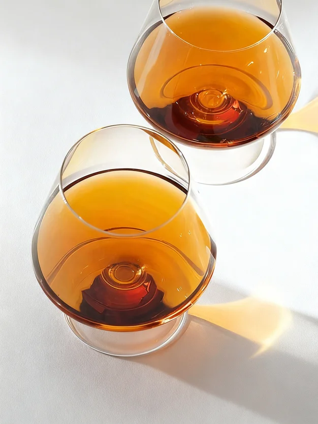 Zwei elegante Cognac Gläser mit bernsteinfarbenem Getränk auf einer glatten, reflektierenden Oberfläche.
