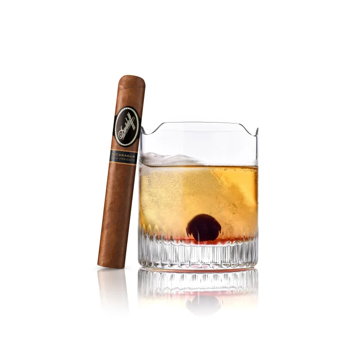 A Davidoff cigar beside a whiskey glass with ice and cherry, exuding refined luxury.