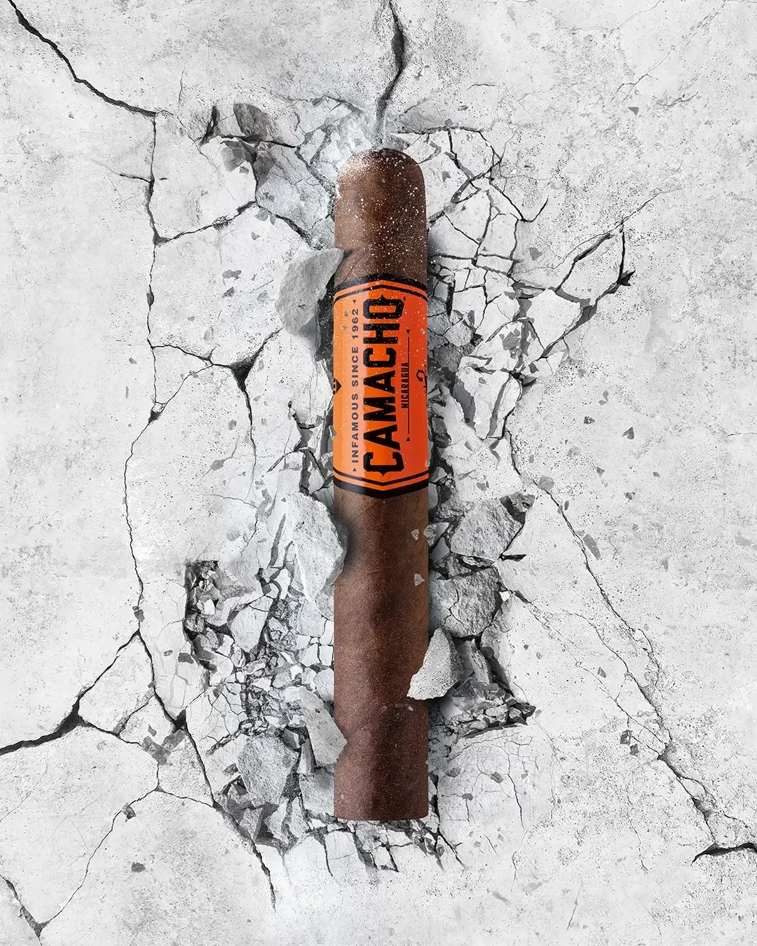 Camacho Nicaragua Zigarre ragt aus rissigem Beton, mit markanter orangener Banderole und kräftigem Erscheinungsbild.