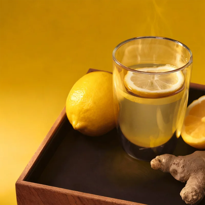 The Davidoff Year of the Snake lancero cigar leaning against a glass of lemon ginger tea next to a lemon and fresh ginger.