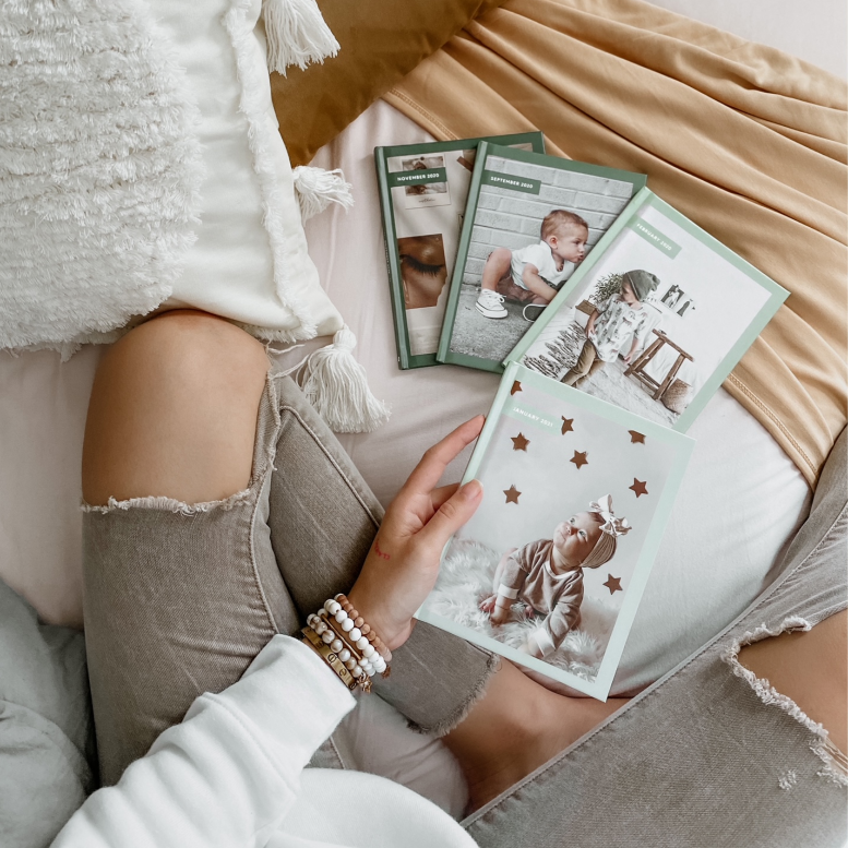 Woman in ripped jeans holding sage ombre Monthbooks by Chatbooks with baby on the cover