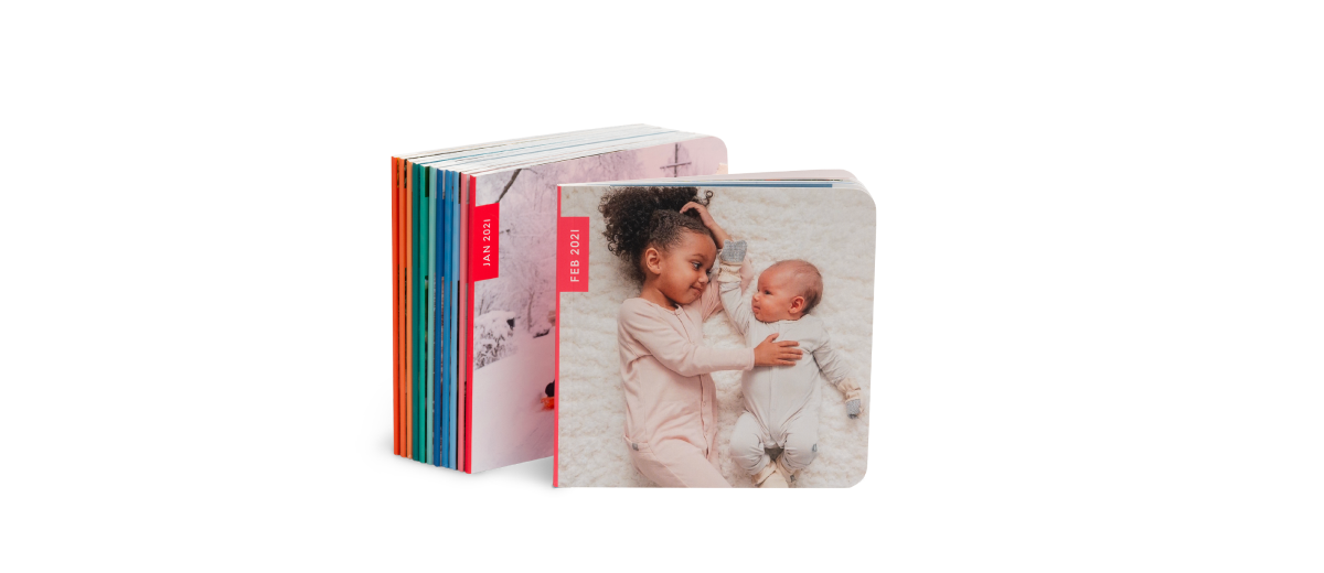 Stack of rainbow baby photo books with a toddler cuddling a baby on the cover