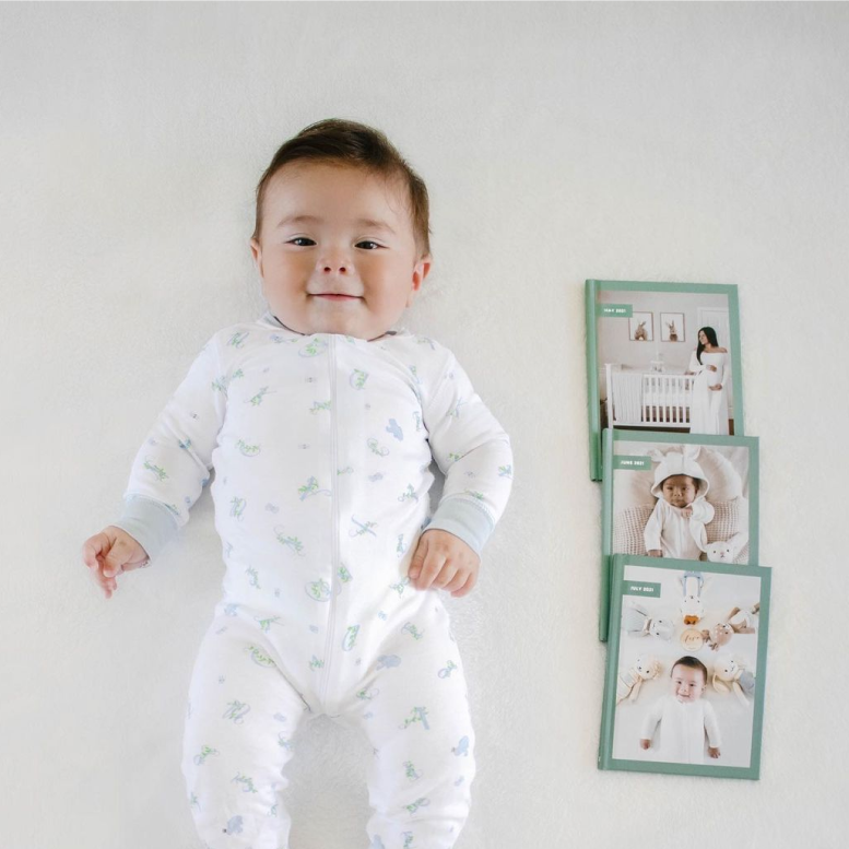 Baby laying next to 3 baby photo albums showing baby growing