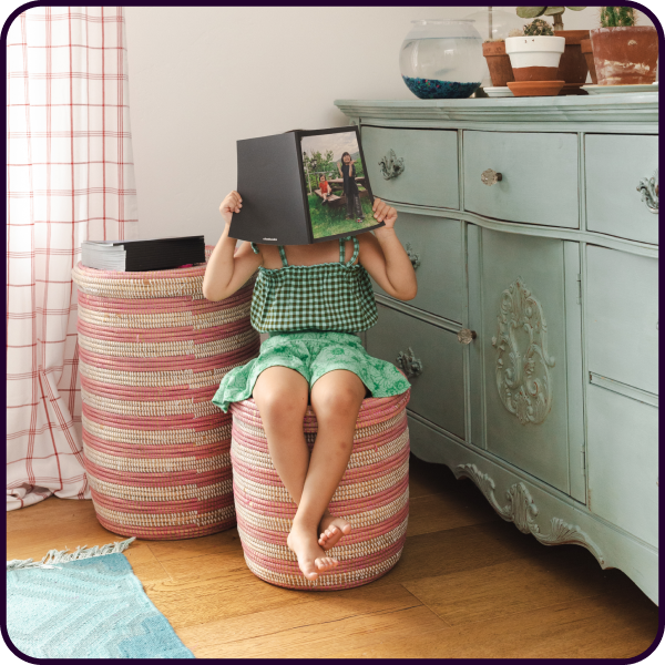 Toddler in bedroom reading a baby photo book with the photo album covering her face