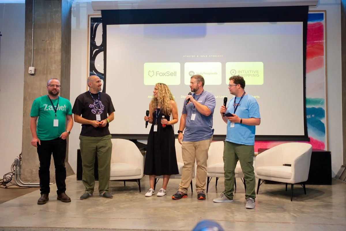 Sam Forde, wearing a green Zapiet t-shirt, stands on stage with four other speakers during the panel at Brightwork Vol.01, with sponsor logos displayed on the screen behind them.