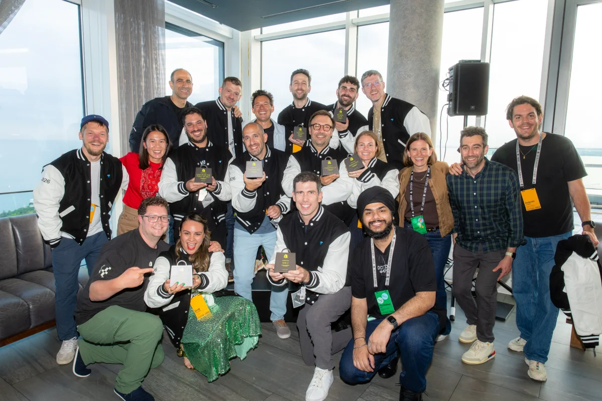 A large group of 2026 Shopify Build Award winners posing together indoors, wearing matching varsity jackets and holding their individual award bags.