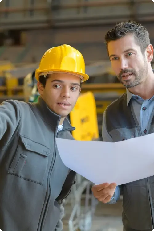 Two men, one in a yellow hardhat, discussing a project. These employees signed a permanent employee agreement when they were hired