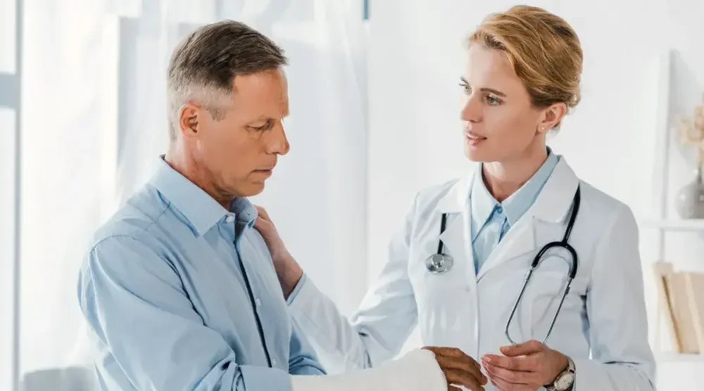 An elderly man with a cast on his right hand speaks with a healthcare professional, discussing the various types healthcare directive and which one is the best for his situation.