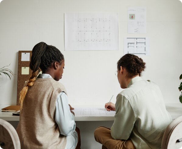 Black woman with braided pony tail wear a brown sweater vest with a white shirt talking to a White male coworker with curly brown hair wearing brown pants and light green shirt sitting in a conference room discussing using LegalZoom for their business dissolution.