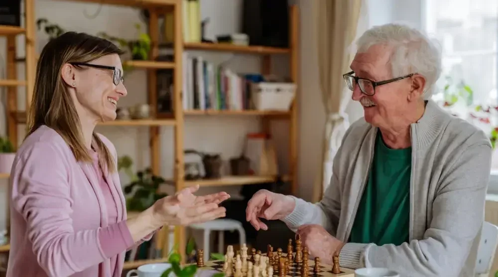 A woman plays chess with her elderly father at his home.