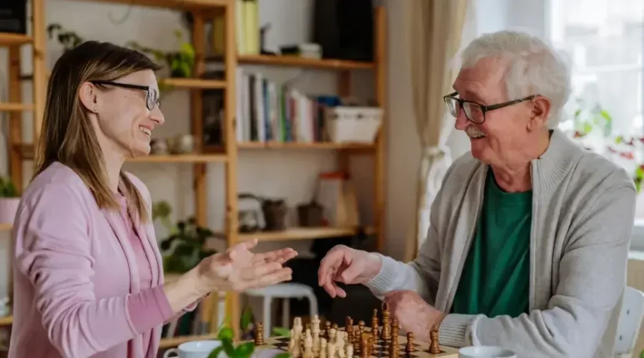 An image of a woman playing chess with her elderly father at his home and discussing how to avoid probate.