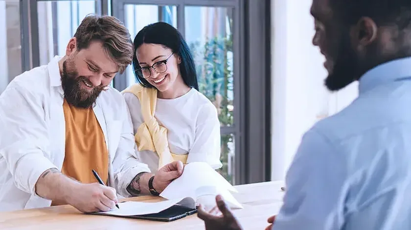 smiling man and woman signing paperwork with an agent
