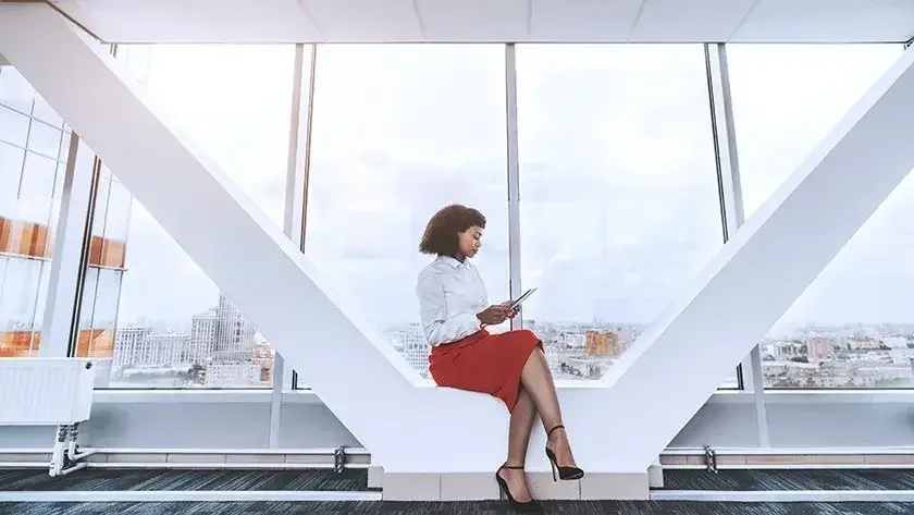 A woman sits in between pillars of a lobby as she reads about LLC formation in New York.