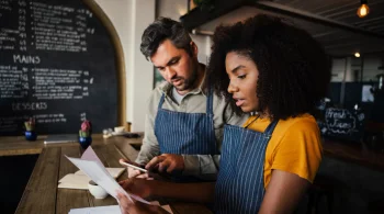 Two people in aprons reviewing documents at a cafe