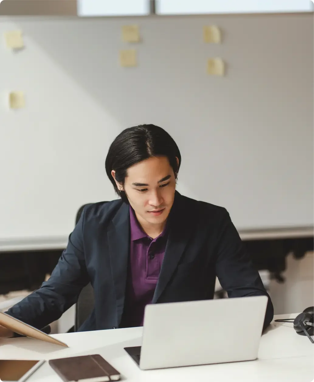 Asian man wearing a black suit jacket over a purple collared shirt working on his LegalZoom business dissolution on his laptop.