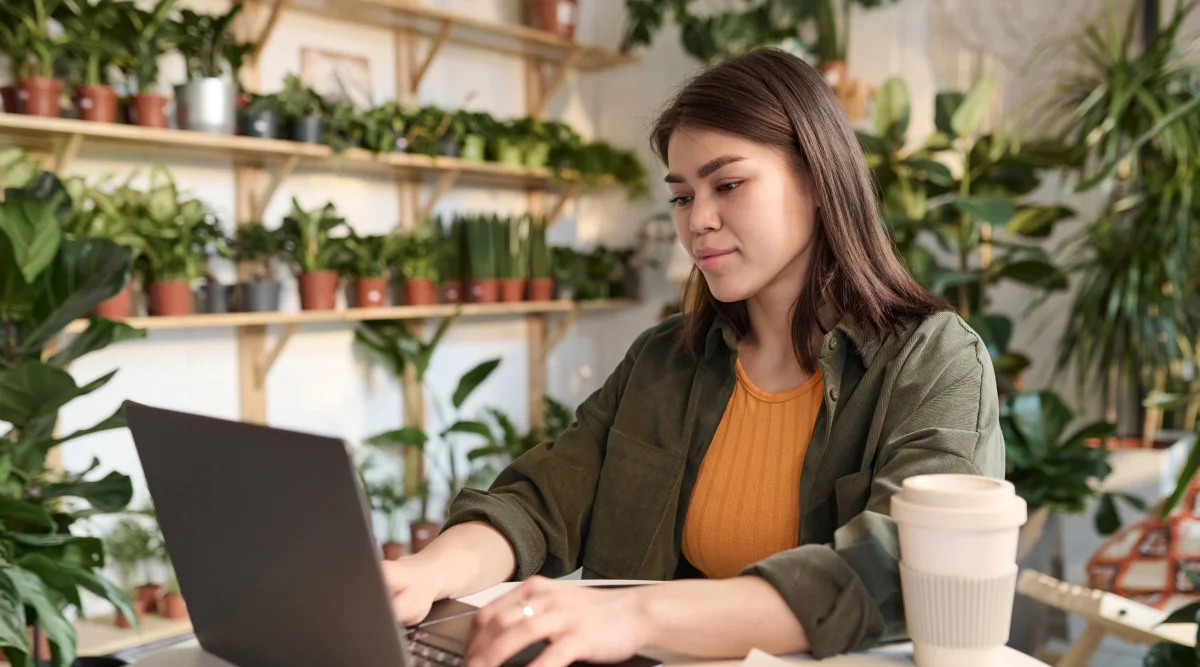 Woman typing on laptop in plant-filled room