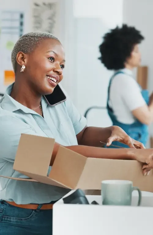 A woman folding cardboard into a box who is on the phone and receiving guidance on employment agreements from an attorney