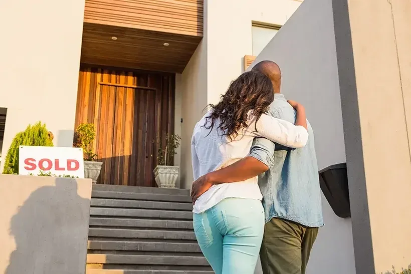 A couple embraces each other as they look up at the home they just purhcased.