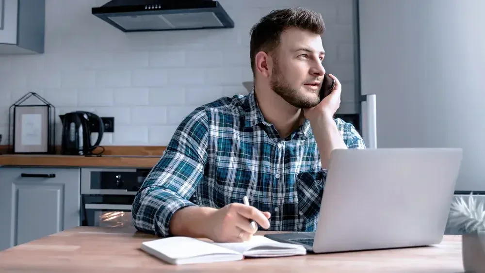 A man talking on the phone and looking out the window in his home office.