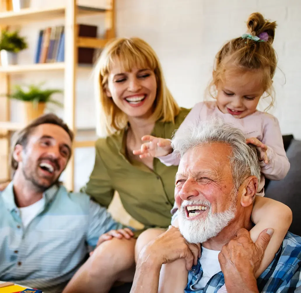 A family playing together. Mom, a blonde woman wearing an olive green button up shirt is smiling watching grandpa, a older man with grey hair and a grey beard smiling as he gives his granddaughter a ride on his shoulders. The little girl is wearing a light pink shirt with her hair in a ponytail. The family is happy that they will be able to avoid probate with a living trust from LegalZoom.