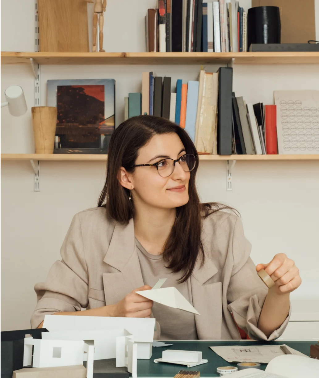 A woman works on a paper rendering at her office desk
