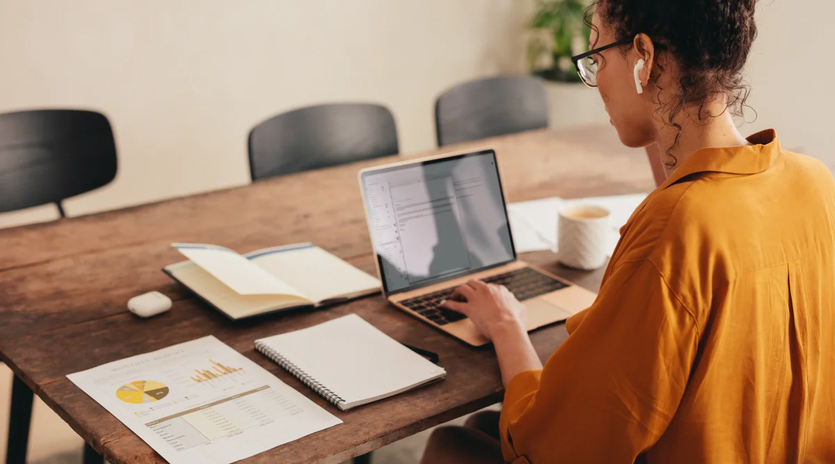 Woman using a laptop with documents on a wooden table