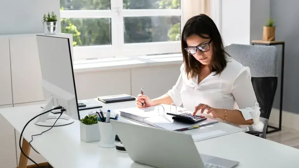 A woman uses a calculator at her desk as she checks her assets, debts, and other income while writing her last will and testament.