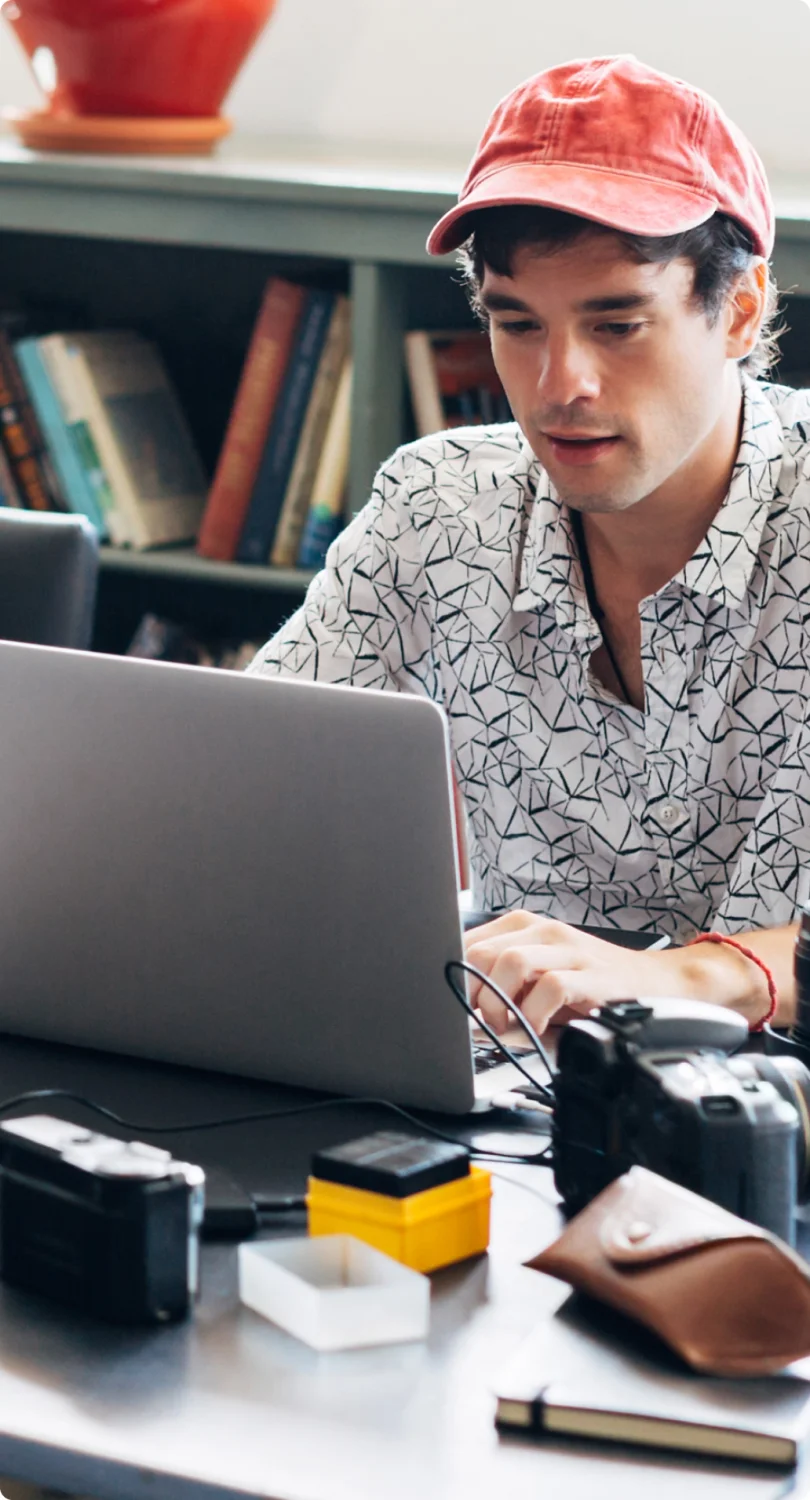 A man in a red baseball cap in front of the laptop