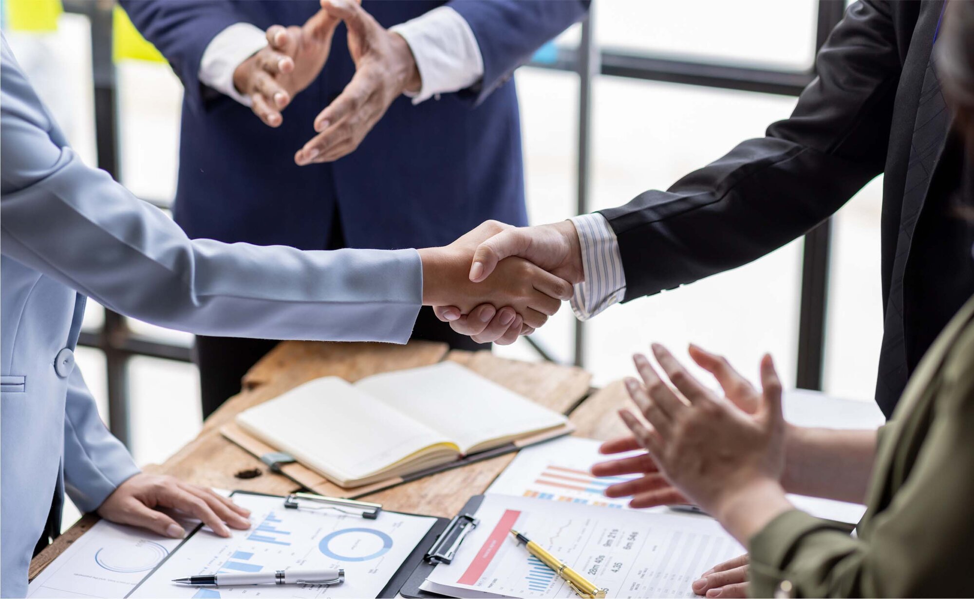 An image of 2 employees shaking hands while others are clapping.