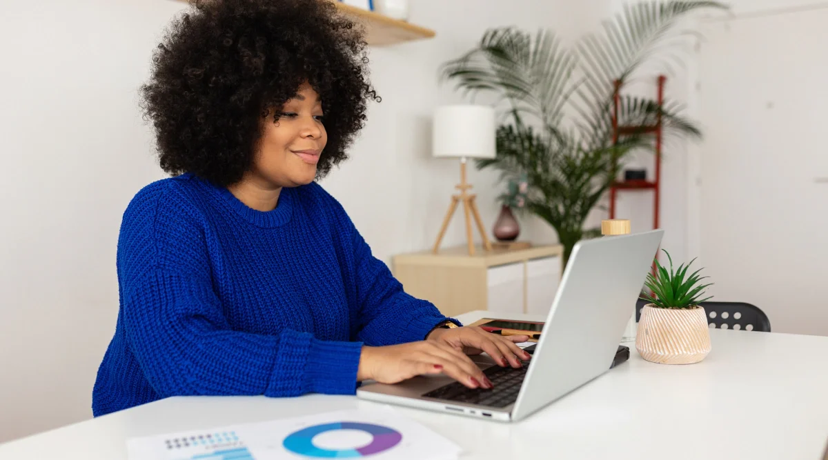 Woman in blue sweater working on laptop happily